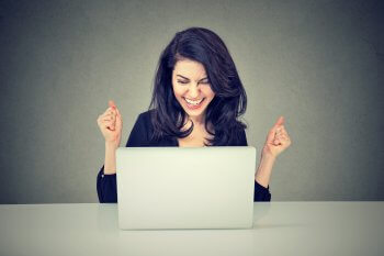 Duales Studium Gehalt junge Frau sitzt vor dem Laptop und freut sich