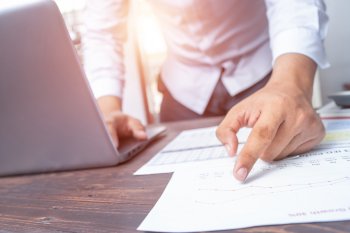 Person steht an Tisch mit Unterlagen und Laptop